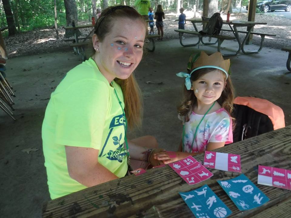 A counselor painting a design on a young camper's hand.