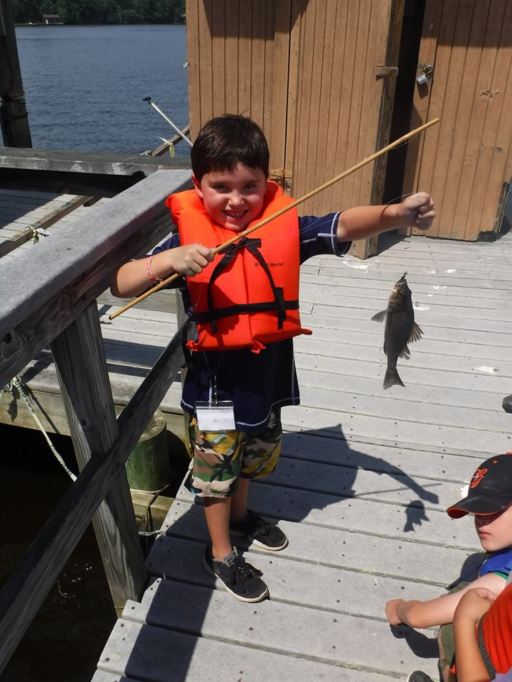A young camper holding a fish on his fishing rod. 
