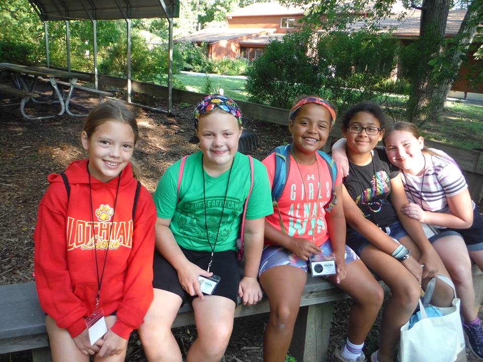 Five campers sitting on a bench and smiling. 