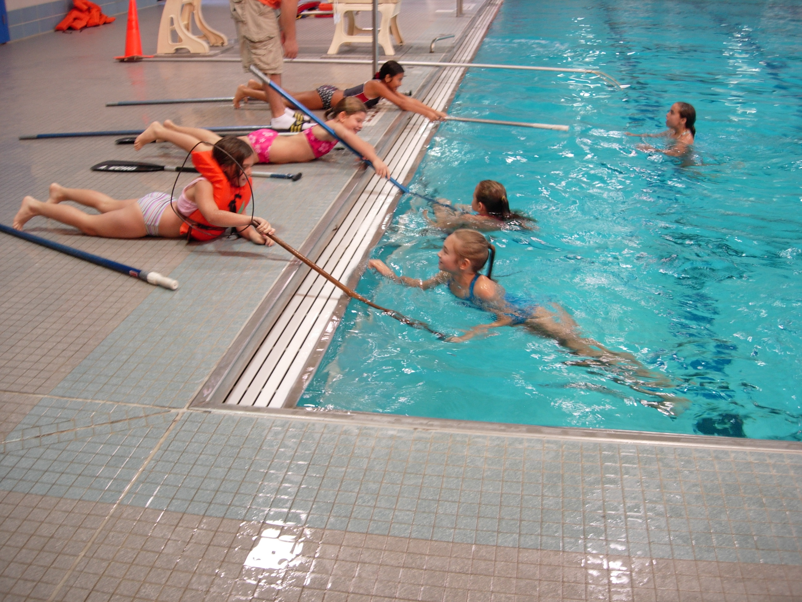 Students laying on the pool deck rescuing partners with a long net.