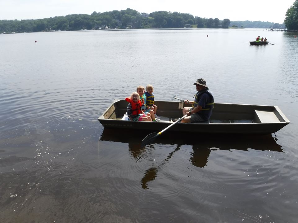 A counselor rowing a row boat with three young campers.