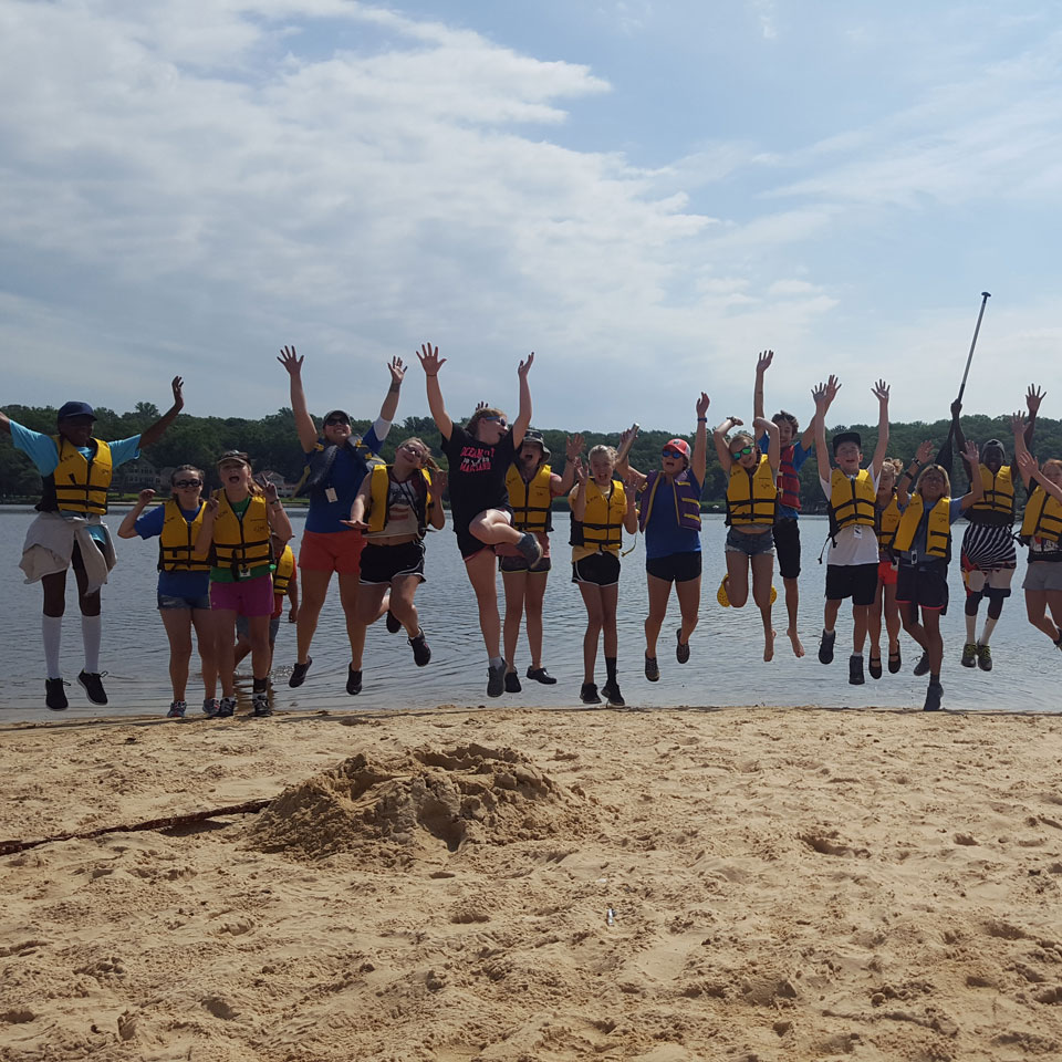 Summer camp kids jump for joy along beach strand.